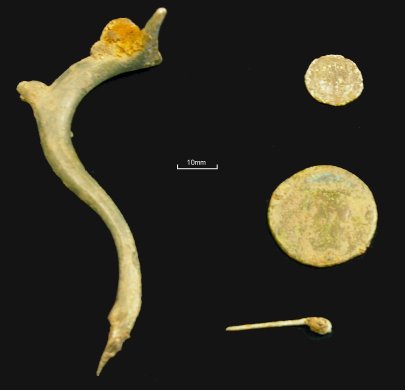 Roman metalwork from the site: (left) the handle from a copper-alloy jug. The handle is a 'dolphin' design and the remaining iron fragment at the top suggests a vessel with a hinged lid. (right, top-bottom) A 3rd/4th century coin, a 1st century coin and a copper-alloy pin.